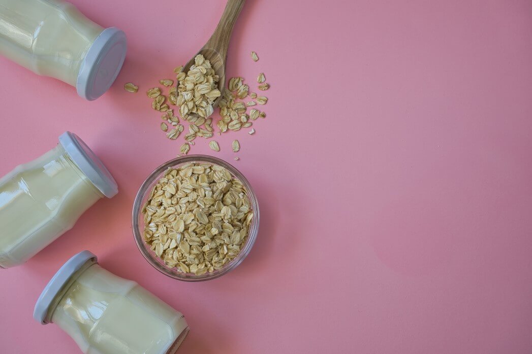 bottles of oat milk and bowl of oats on pink background
