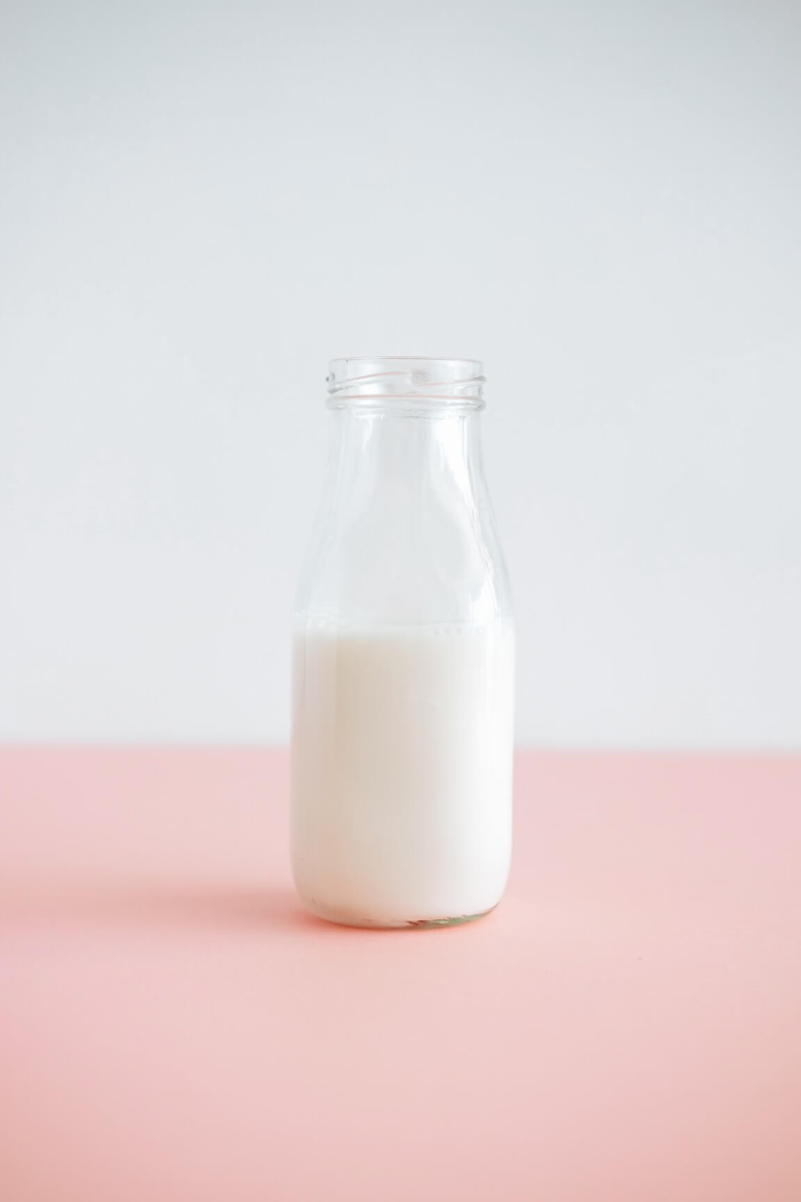glass of milk in bottle on pink table