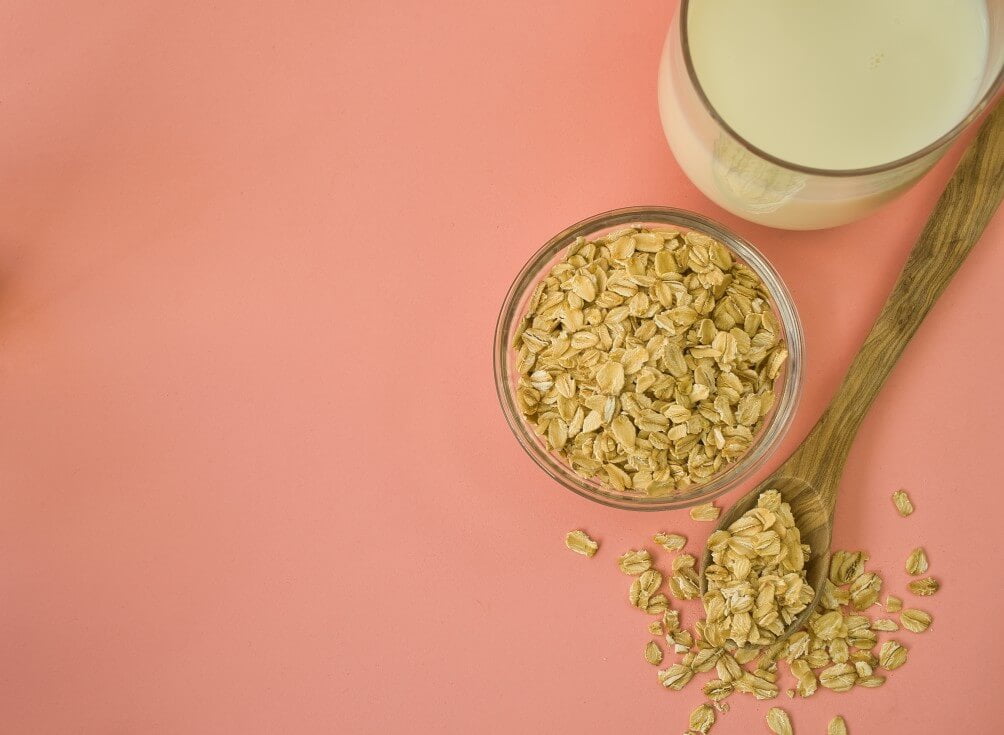 glass of oat milk and bowl of oats on pastel background