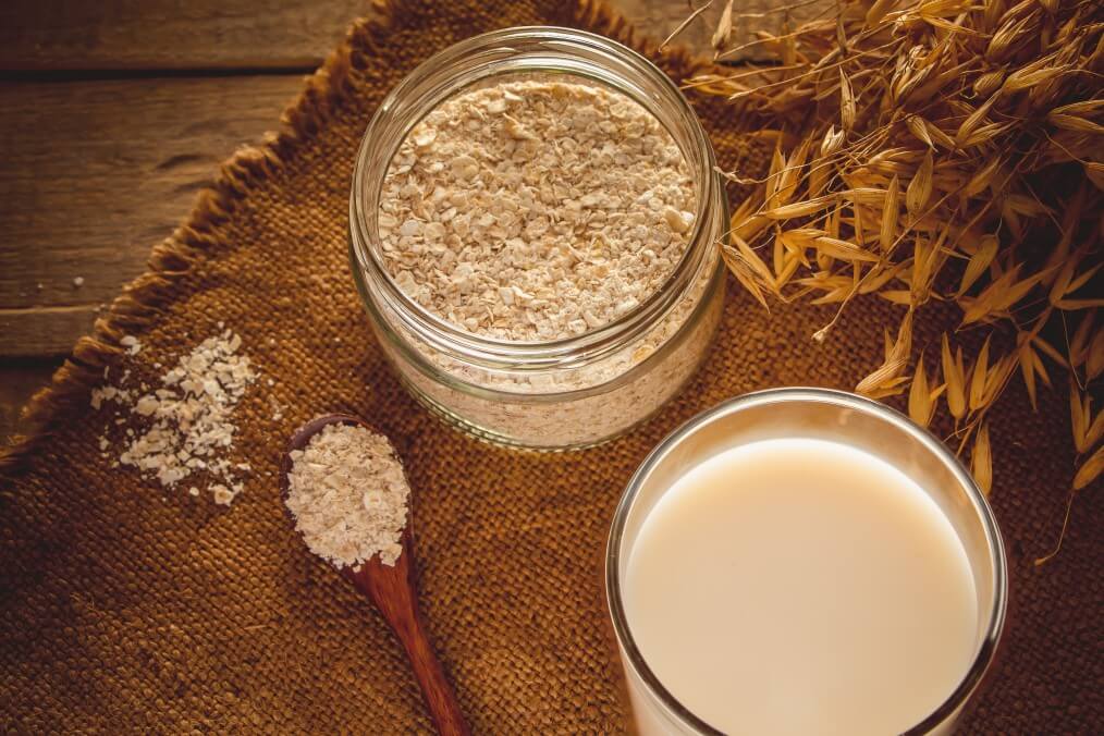 glass of oat milk and jar of oats next to grains