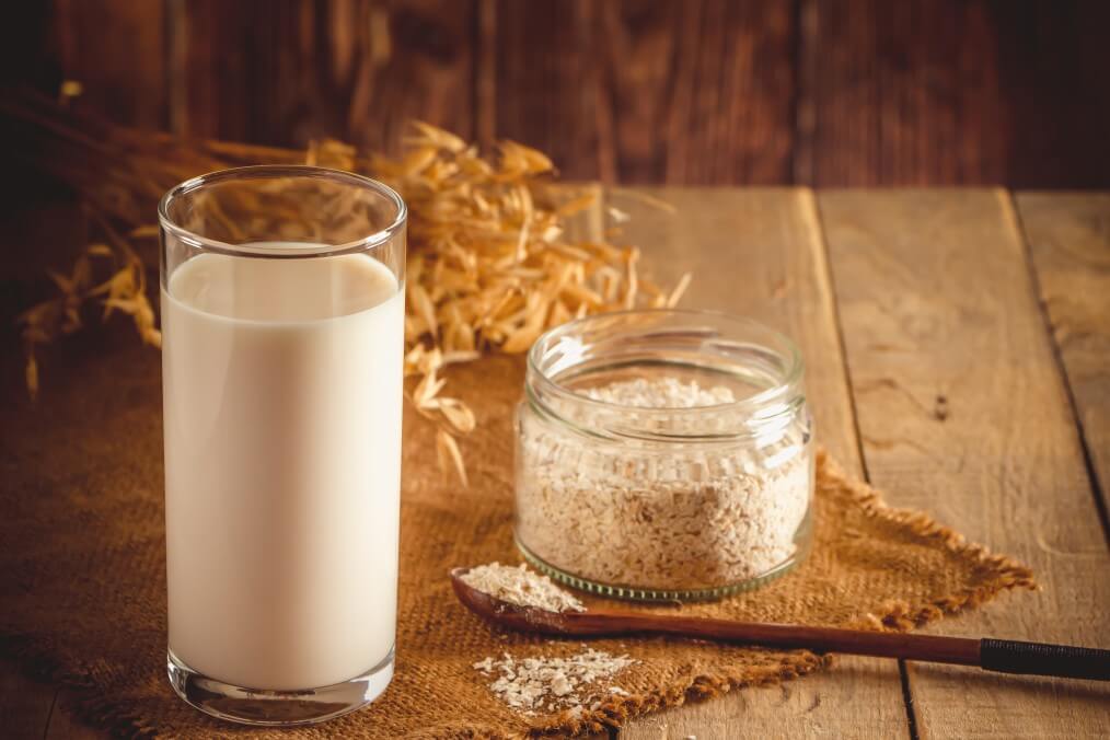glass of oat milk on wooden background and jar of oats