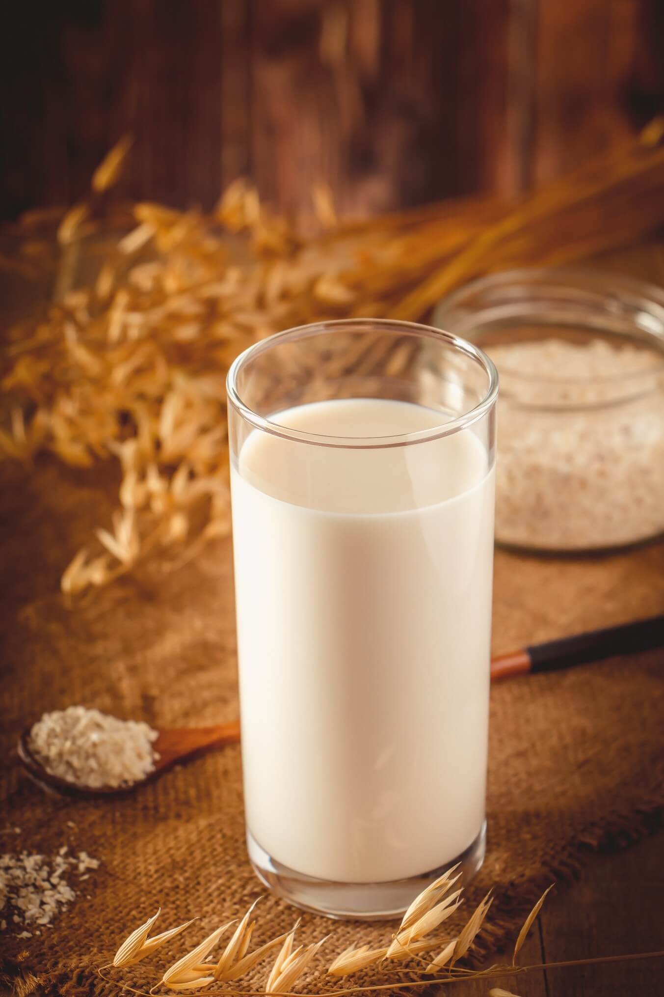 glass of oat milk on wooden background with grains