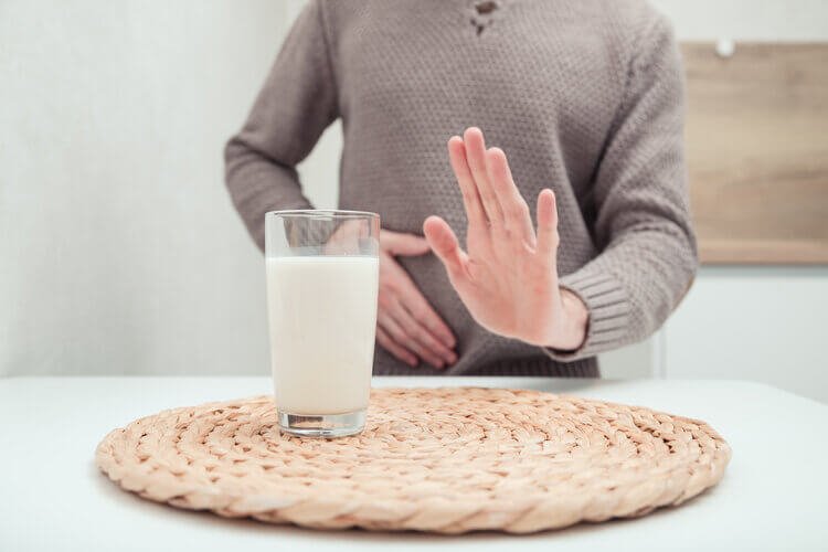 man holding stomach with glass of milk on table
