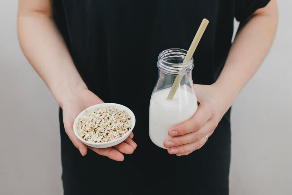 man in black shirt holding bottle of oat milk and bowl of oat flakes