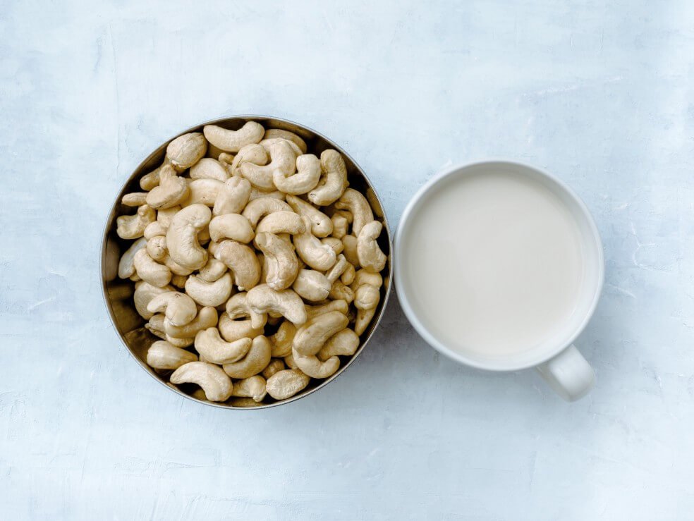 mug of cashew milk next to bowl of cashews