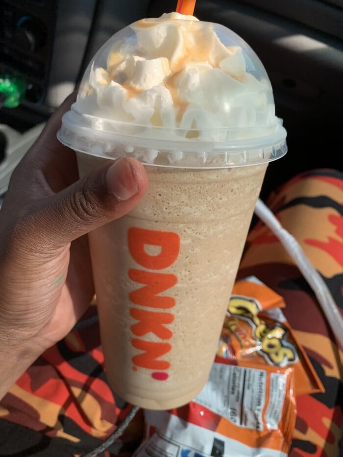 person holding dunkin donuts drink with whipped cream