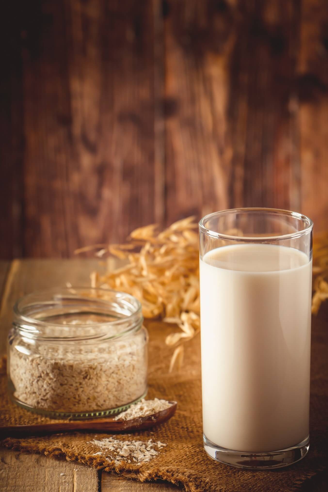 tall glass of oat milk with jar of oats and grains in background