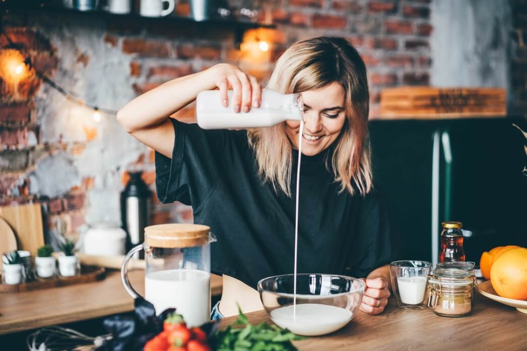 woman pouring oat milk into clear bowl in a kitchen