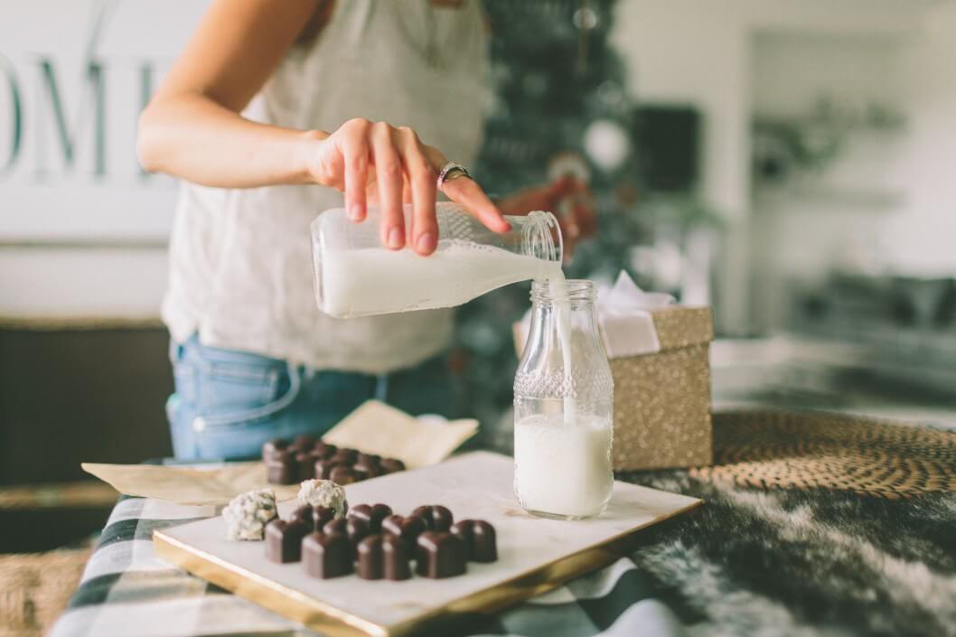woman pouring milk into glass bottle with chocolates on table