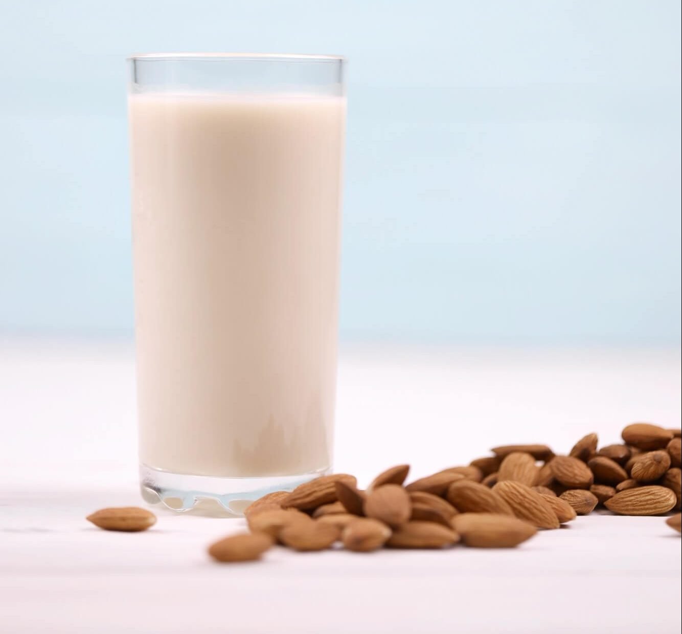 Glass of almond milk with almond nuts on white wooden table