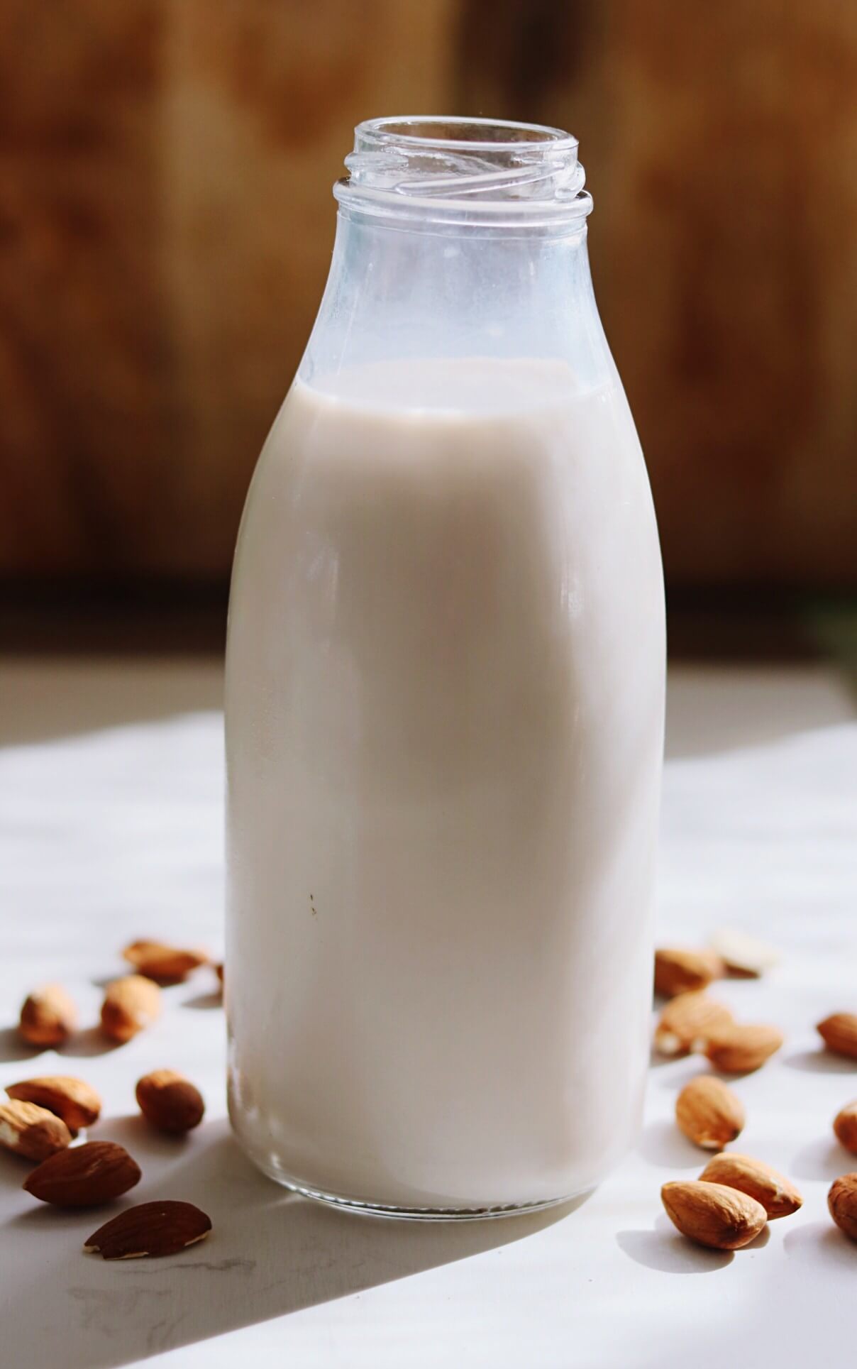 almond milk in milk bottle on table surrounded by almonds