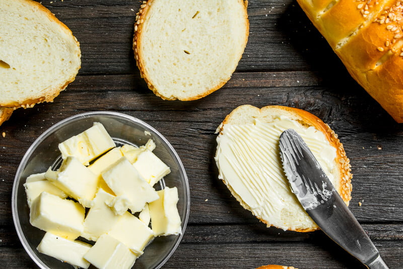 bowl of butter pieces next to sliced bread with butter spread