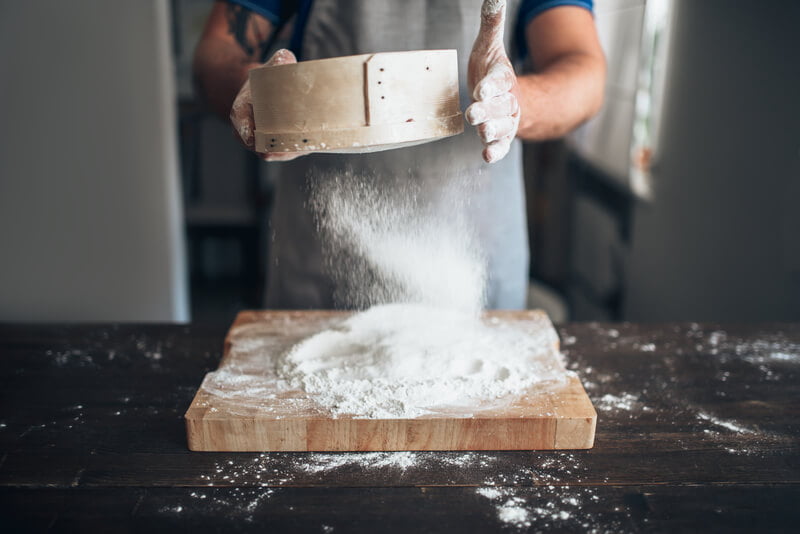 chef sifting flour onto cutting board