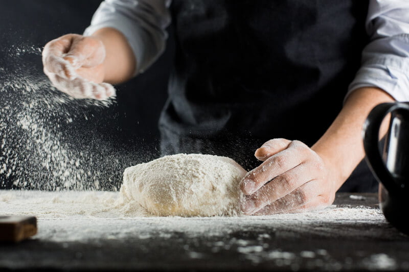 chef throwing flour on dough