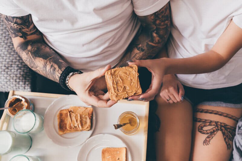 couple holding peanut butter on bread with glasses of milk on tray