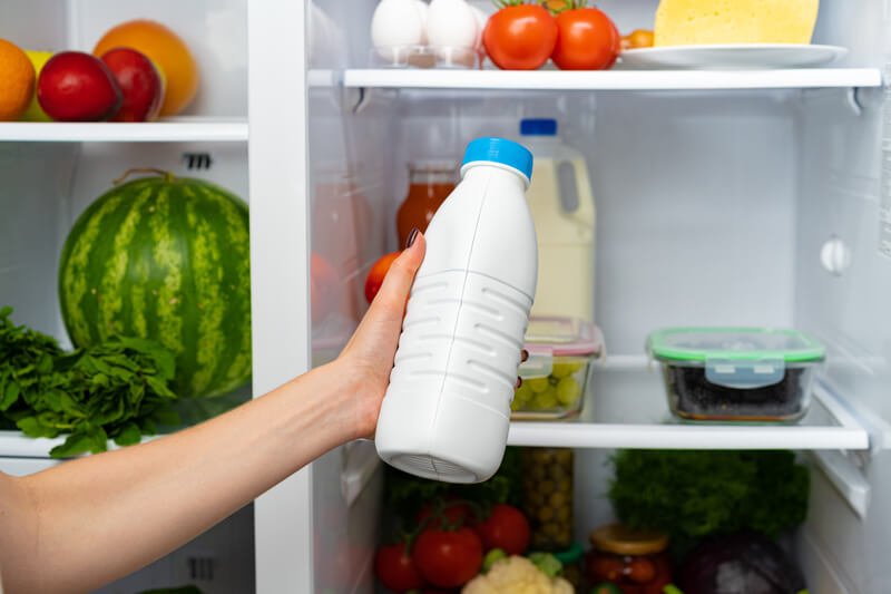 female hand taking bottle of milk from fridge