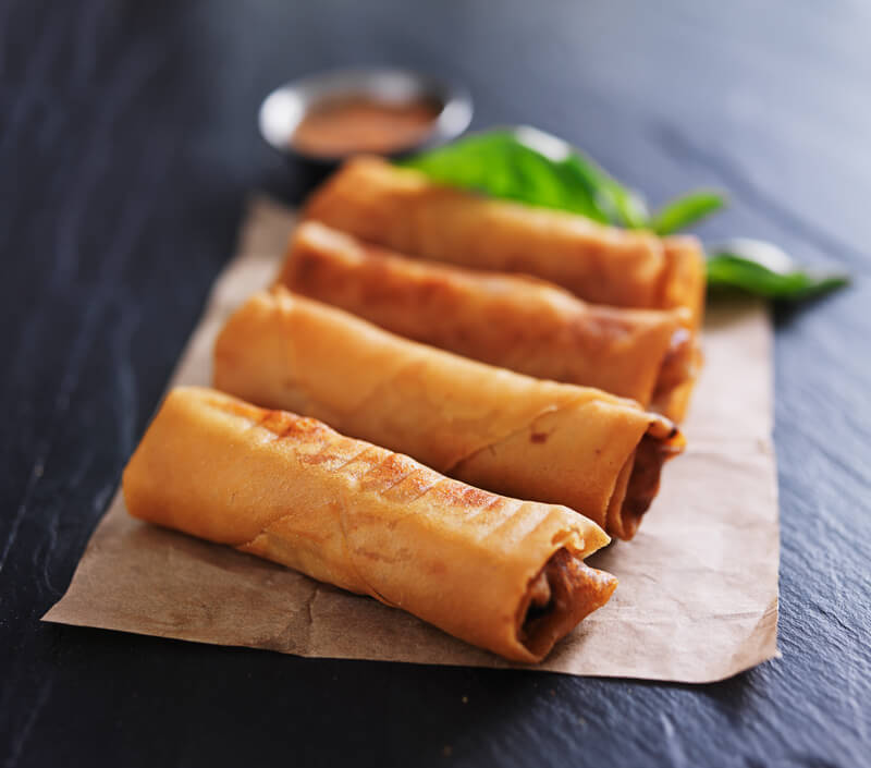 four eggrolls on paper with sauce in background