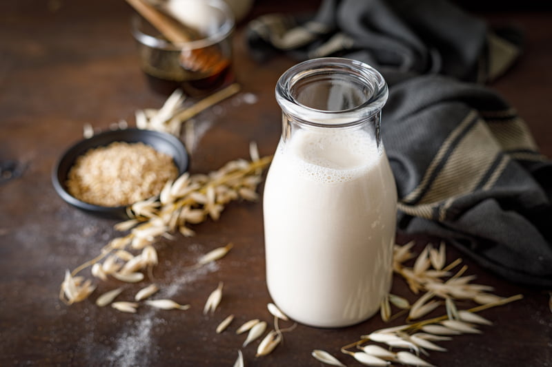 Vegan oat milk in glass bottle and ingredients for cooking