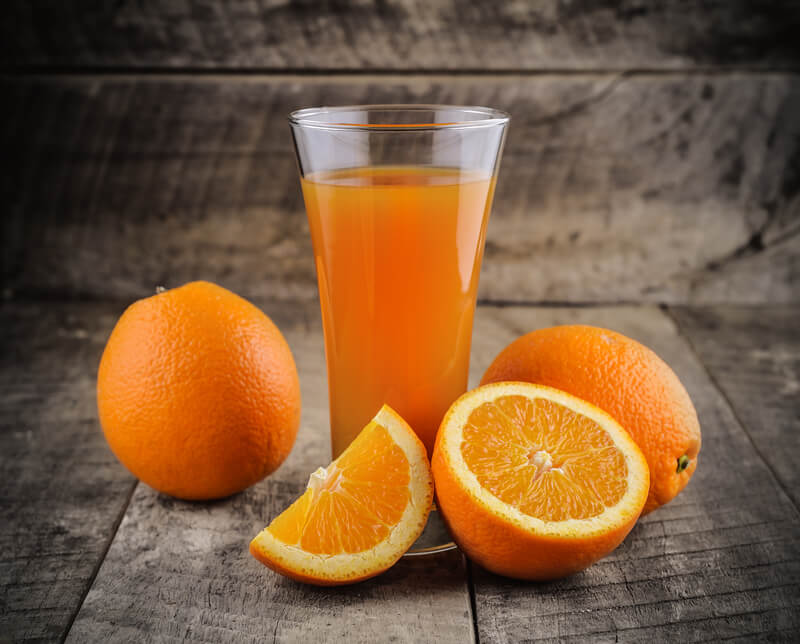 glass of orange juice surrounded by oranges