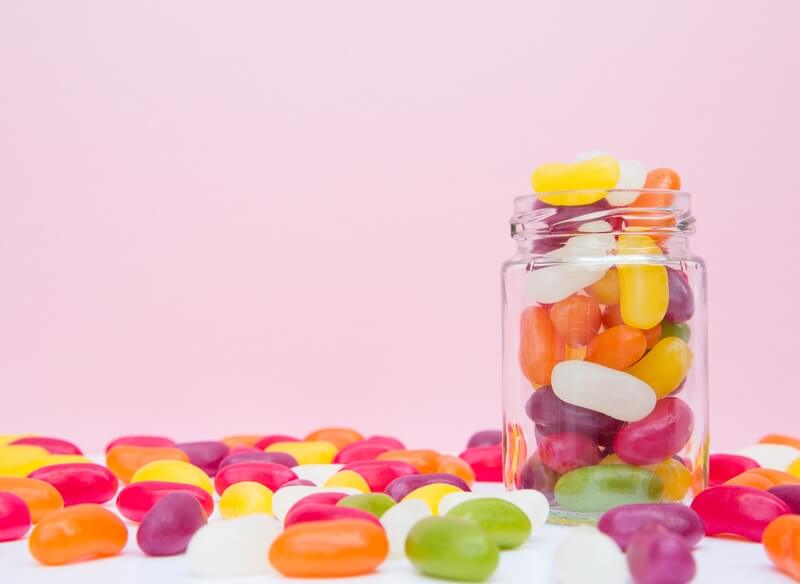 jar of jelly beans with scattered jelly beans on table with pink background