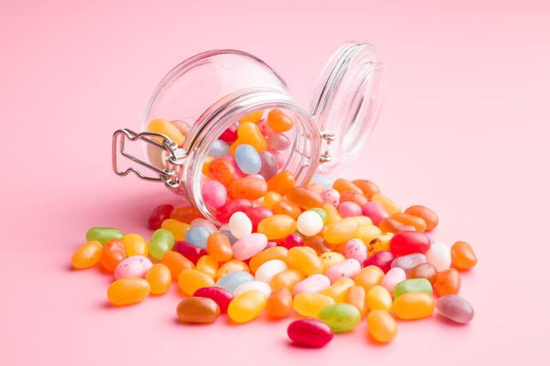 jelly beans falling out of glass jar with pink background