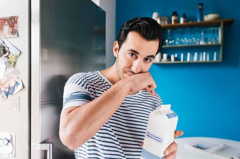 man wiping mouth after drinking from milk carton