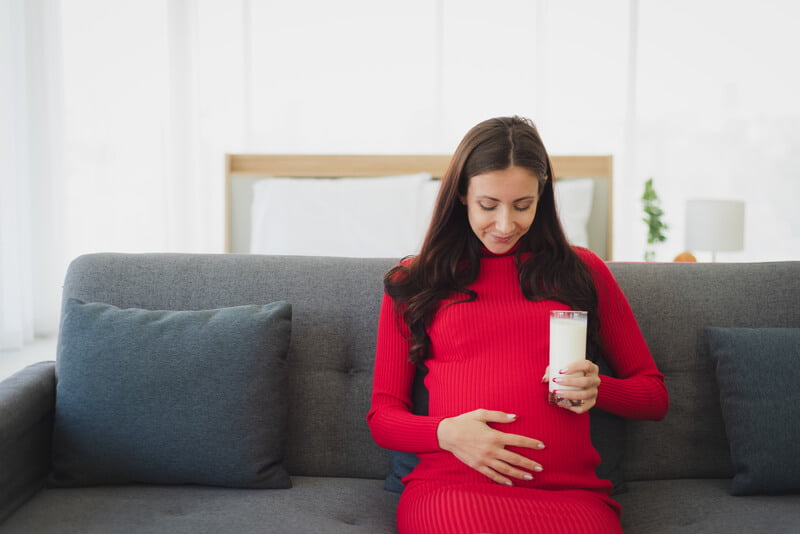pregnant woman in red dress on couch drinking milk