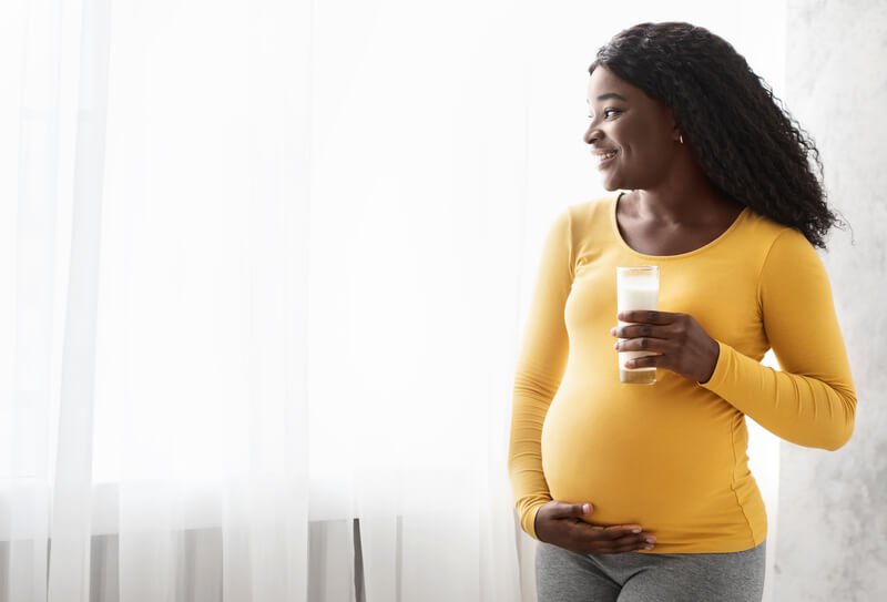 pregnant woman with yellow shirt holding glass of milk