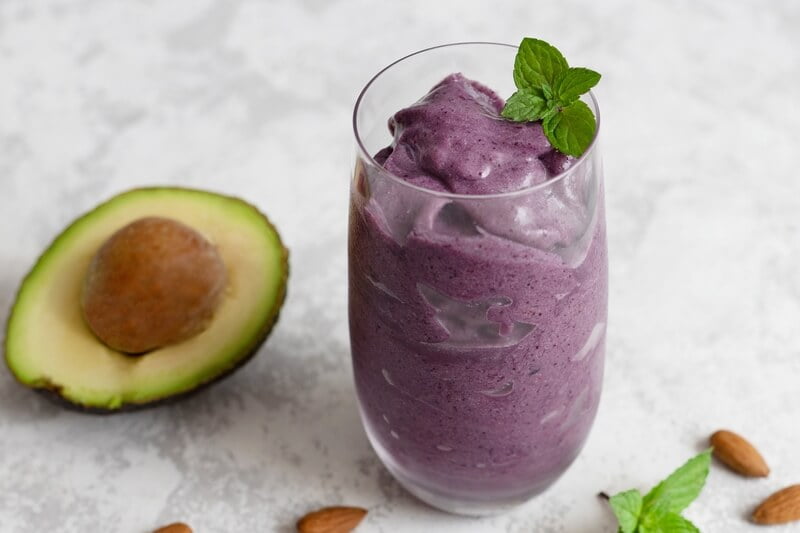 purple smoothies in glass next to avocado