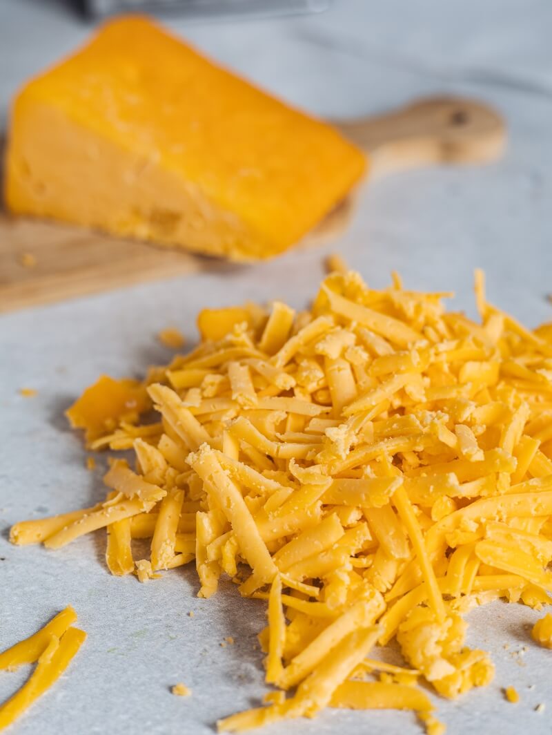 shredded cheddar cheese with block of cheese in background