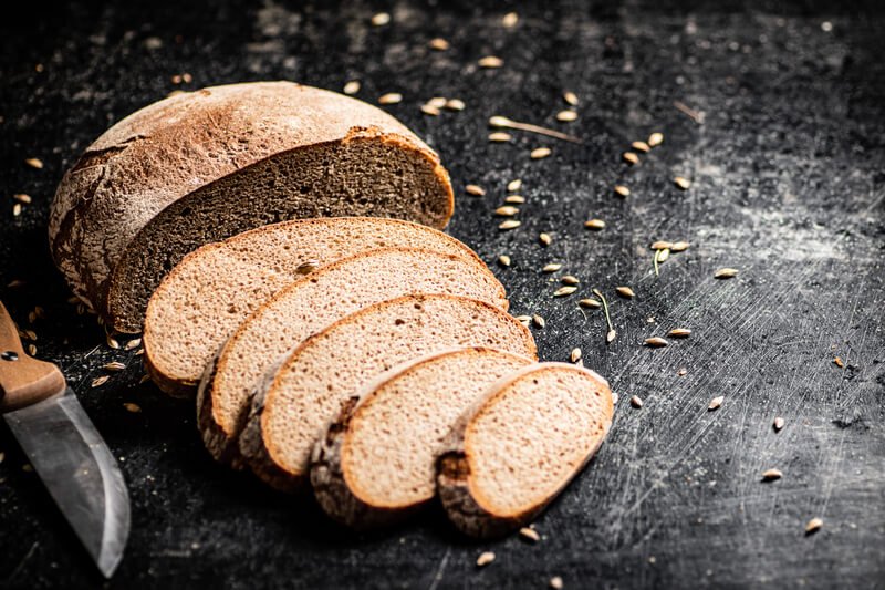 sliced loaf of bread on dark table with seeds scattered