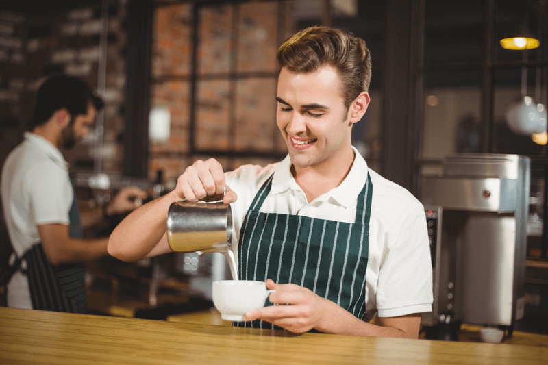 smiling barista pouring milk in coffee cup at coffee shop