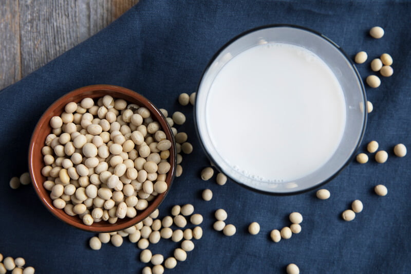 soy milk and soy beans laying flat on blue background