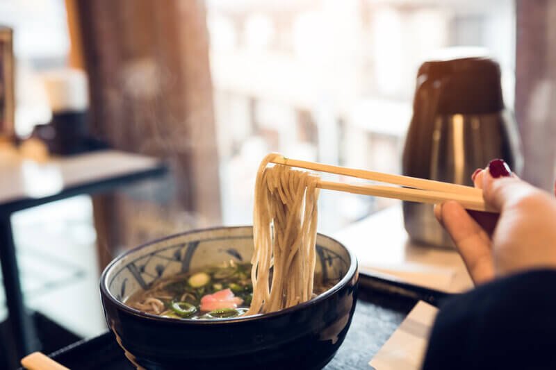 woman eating ramen noodles from bowl in restaurant