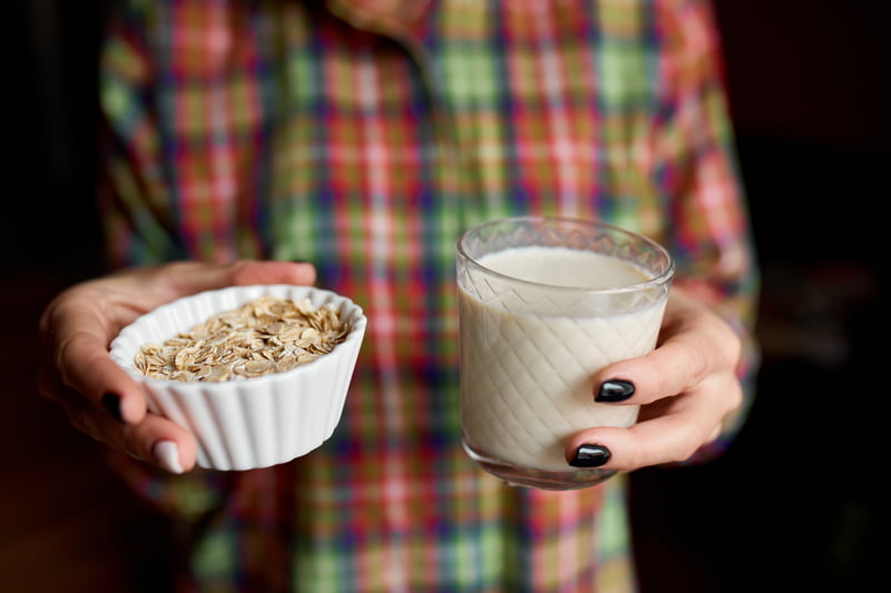 woman holding class of oat milk and bowl of oats