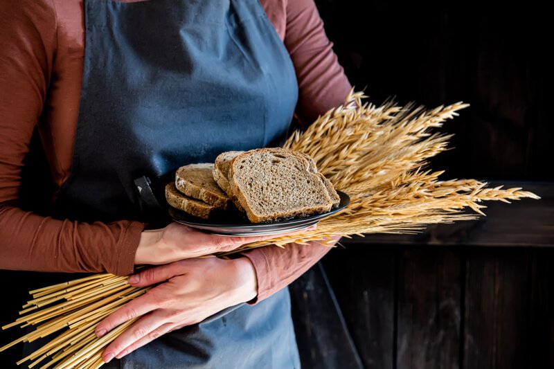 woman in apron holding sliced wheat bread and grains