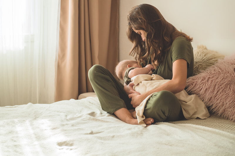 woman breastfeeding baby sitting on bed