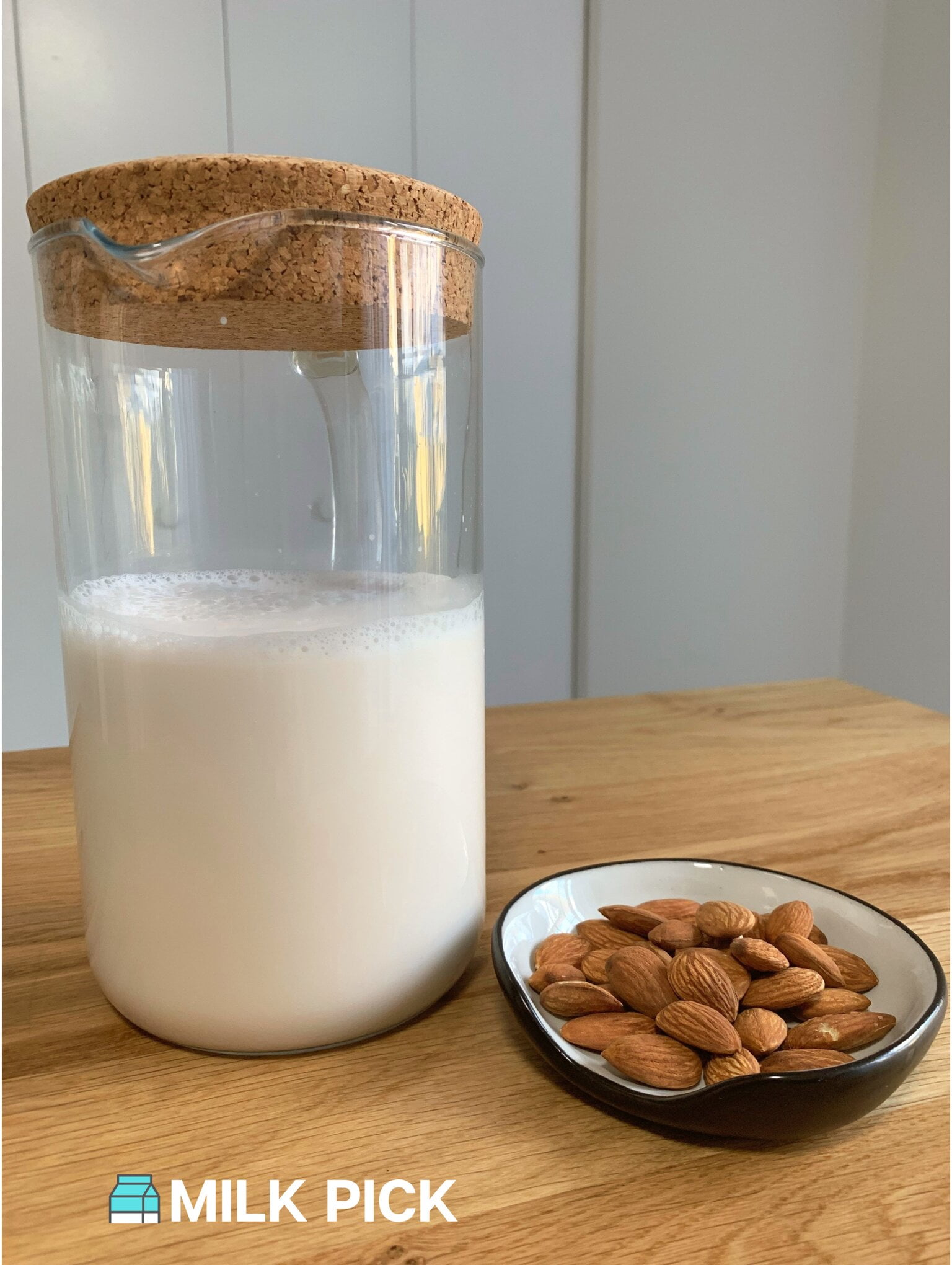 homemade almond milk in glass pitcher next to bowl of almonds