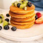 stack of almond milk pancakes topped with fruit on plate