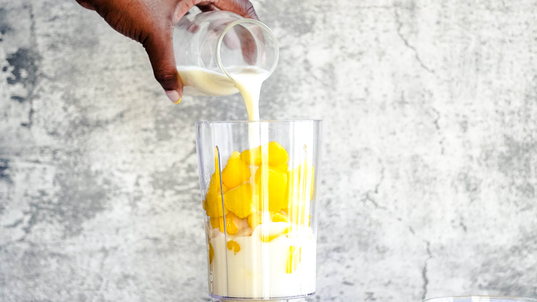 pouring coconut yogurt into dairy-free mango smoothie